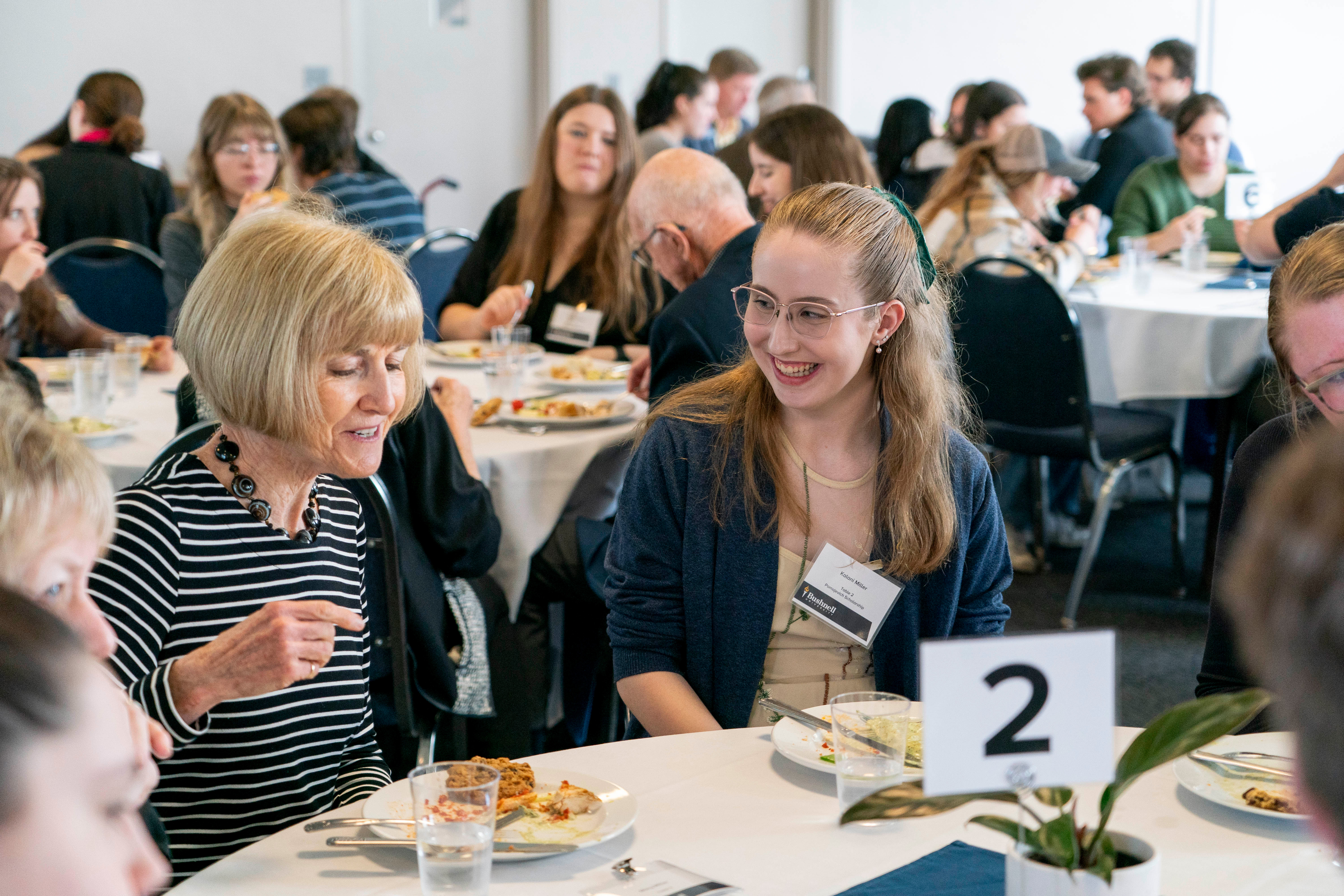 Student with glasses and scholarship donor smiling at a luncheon event.