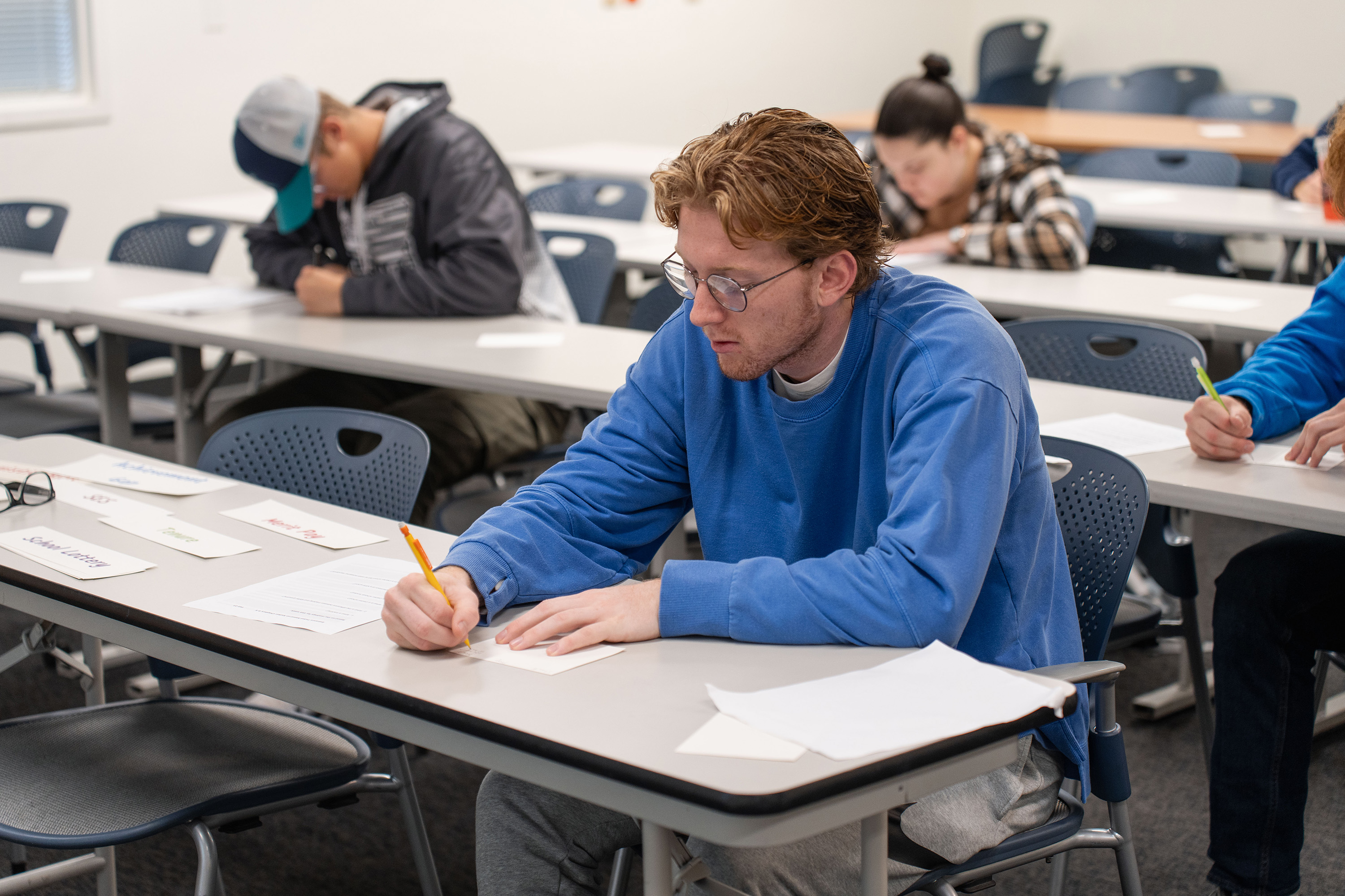 Student in classroom setting concentrates on a written assessment.