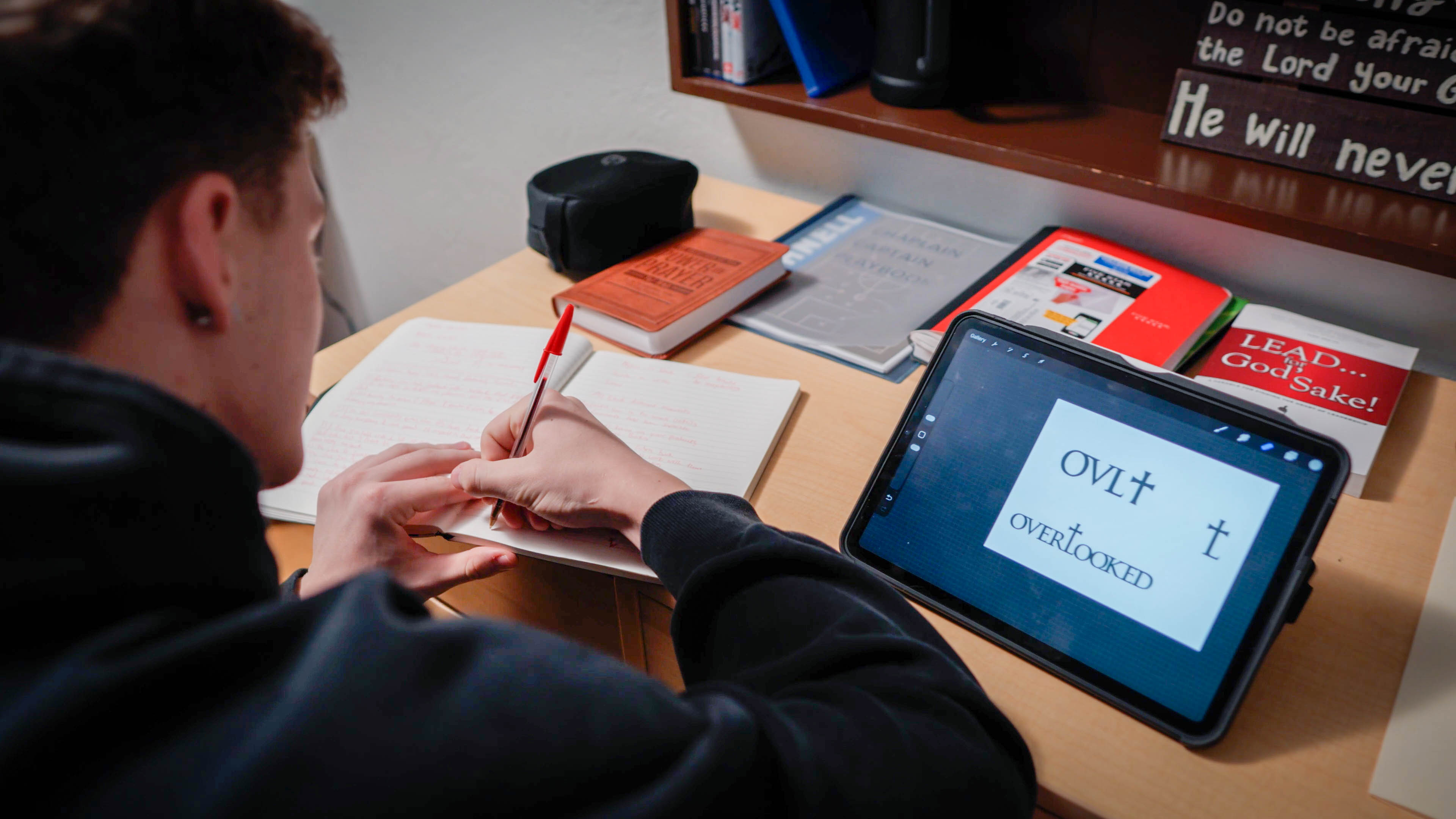Bushnell University student sketches ideas in a notebook while creating a digital design project on a tablet.