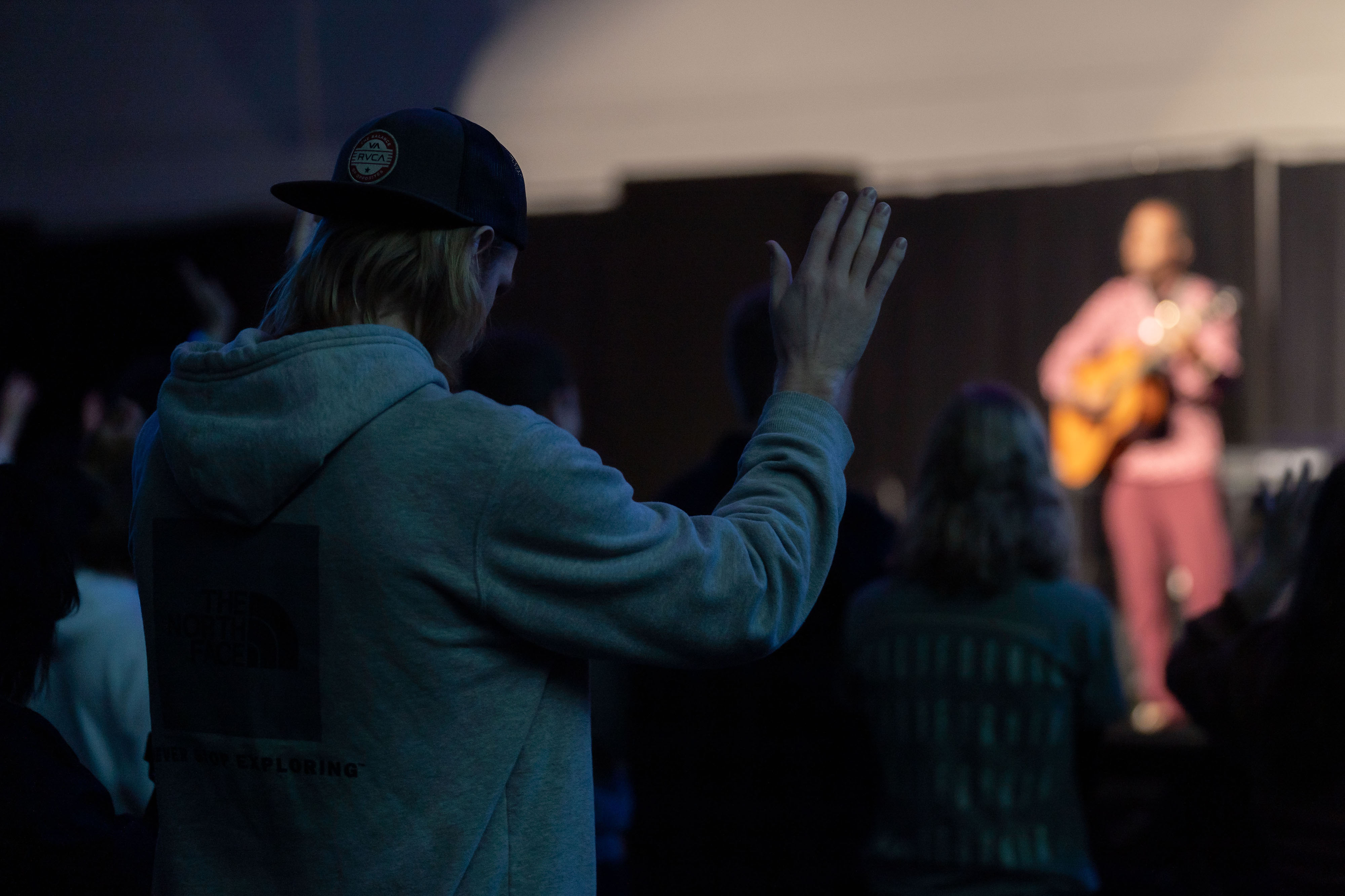 Photo taken behind a student with a hand raised in worship during chapel.