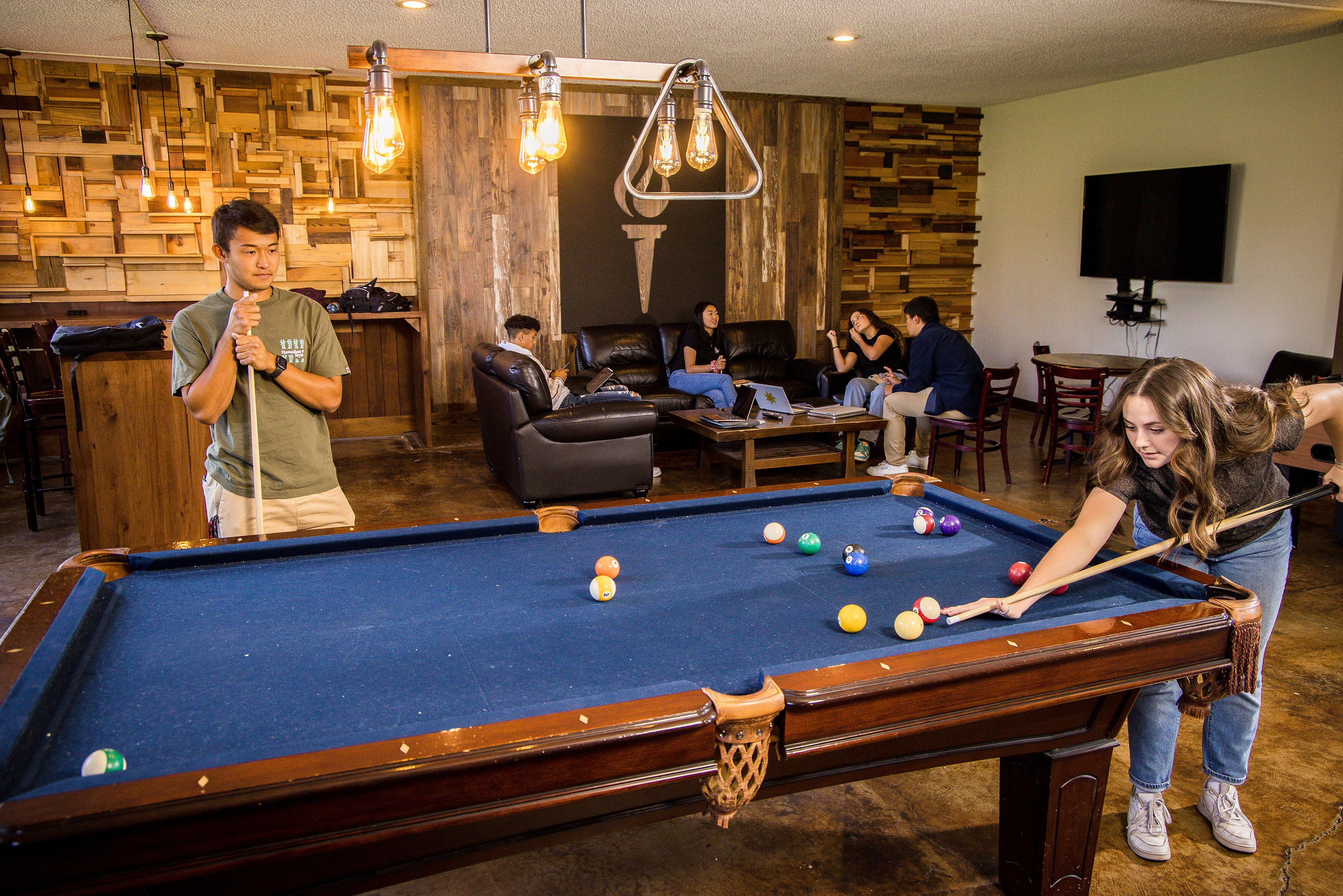 A group of students in a Bushnell University dorm building play pool and hang out in a recreation room.