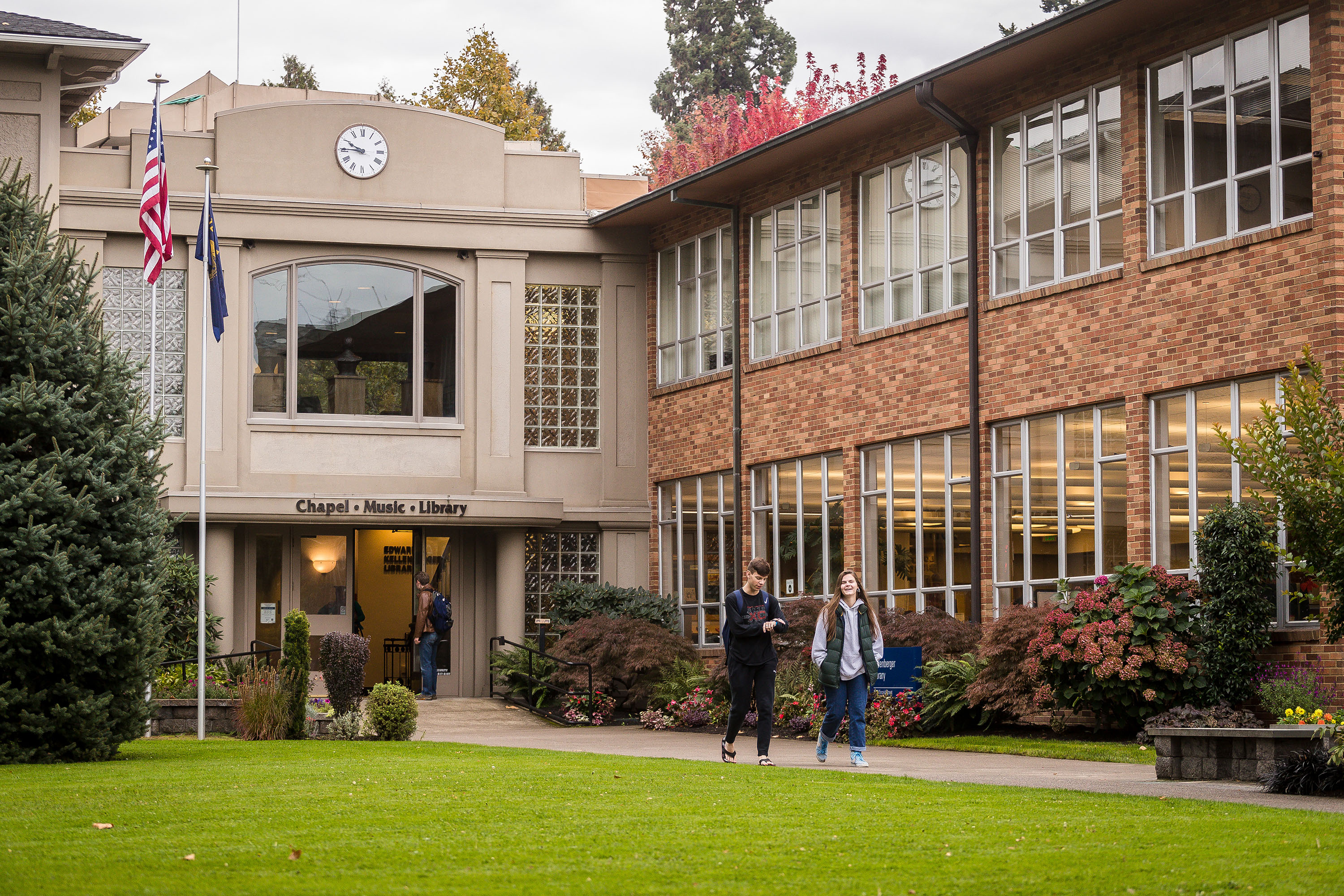 Bushnell University students walking on campus in front of the brick library building and music hall.