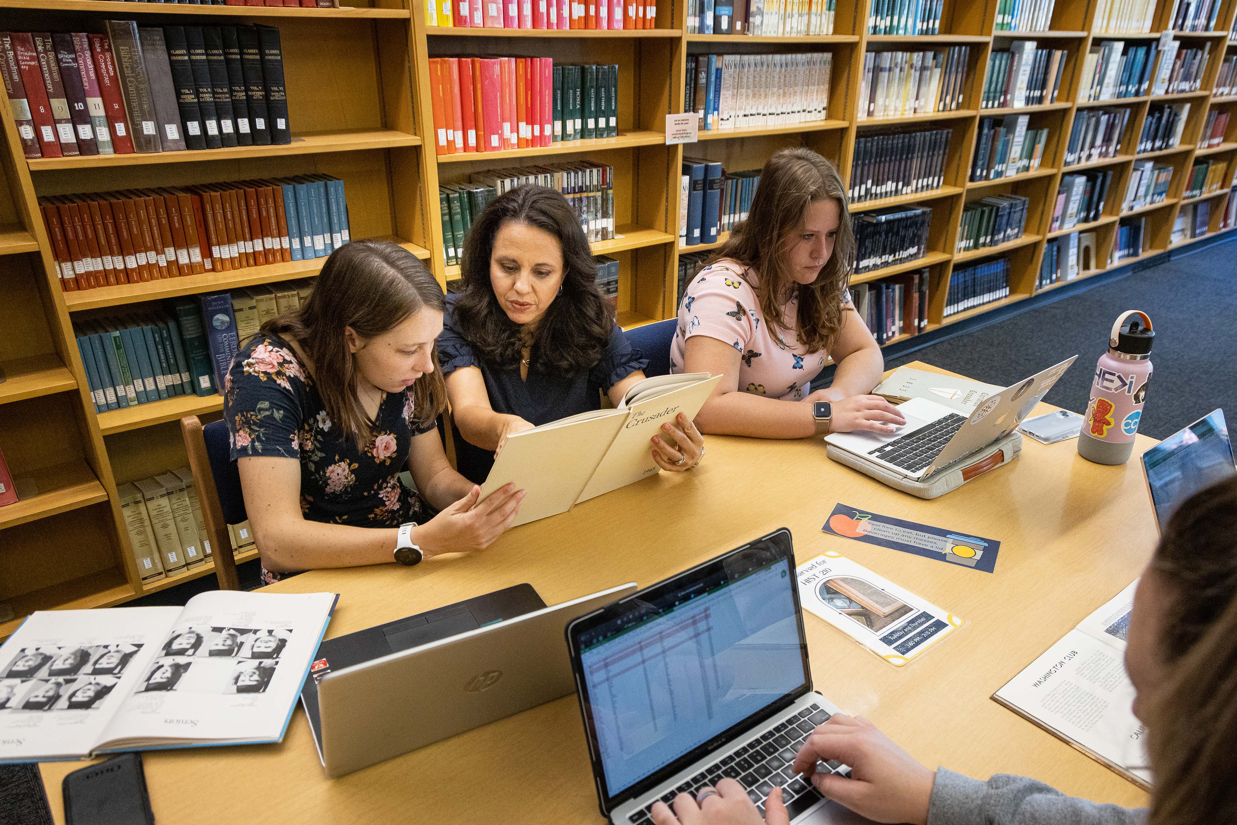 An accessibility assistant and teacher helps a student read through an old university yearbook.