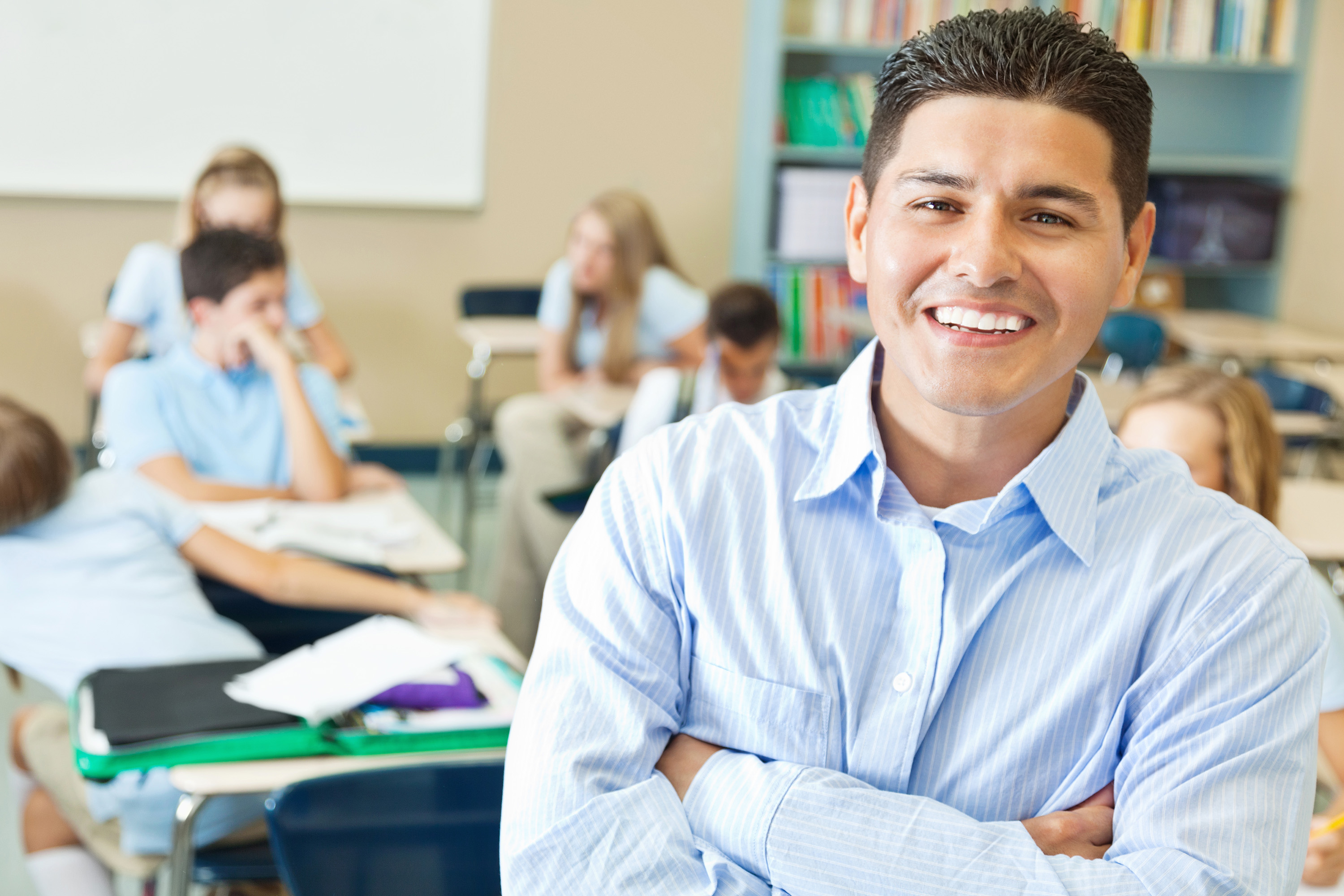 Teacher smiles in class while students study behind them.