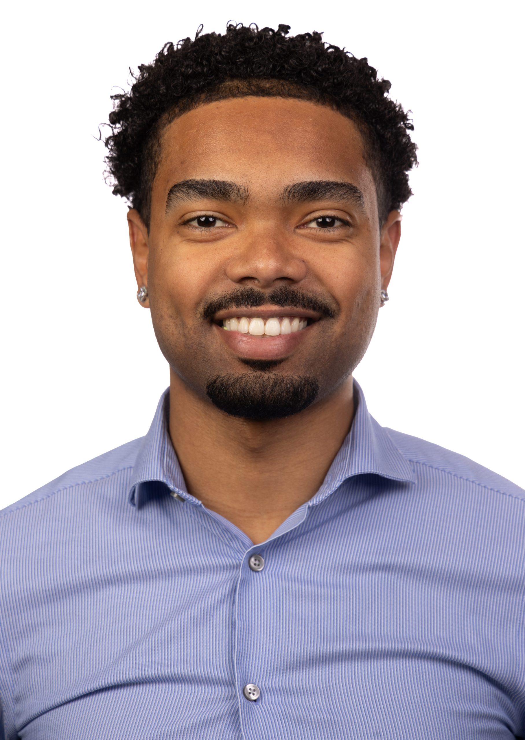 Portrait of a smiling man with short curly dark hair and a trimmed goatee wearing a light blue collared shirt against a white background.