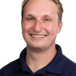 Portrait of a smiling man with short light brown hair wearing a navy Bushnell University polo shirt against a white background.