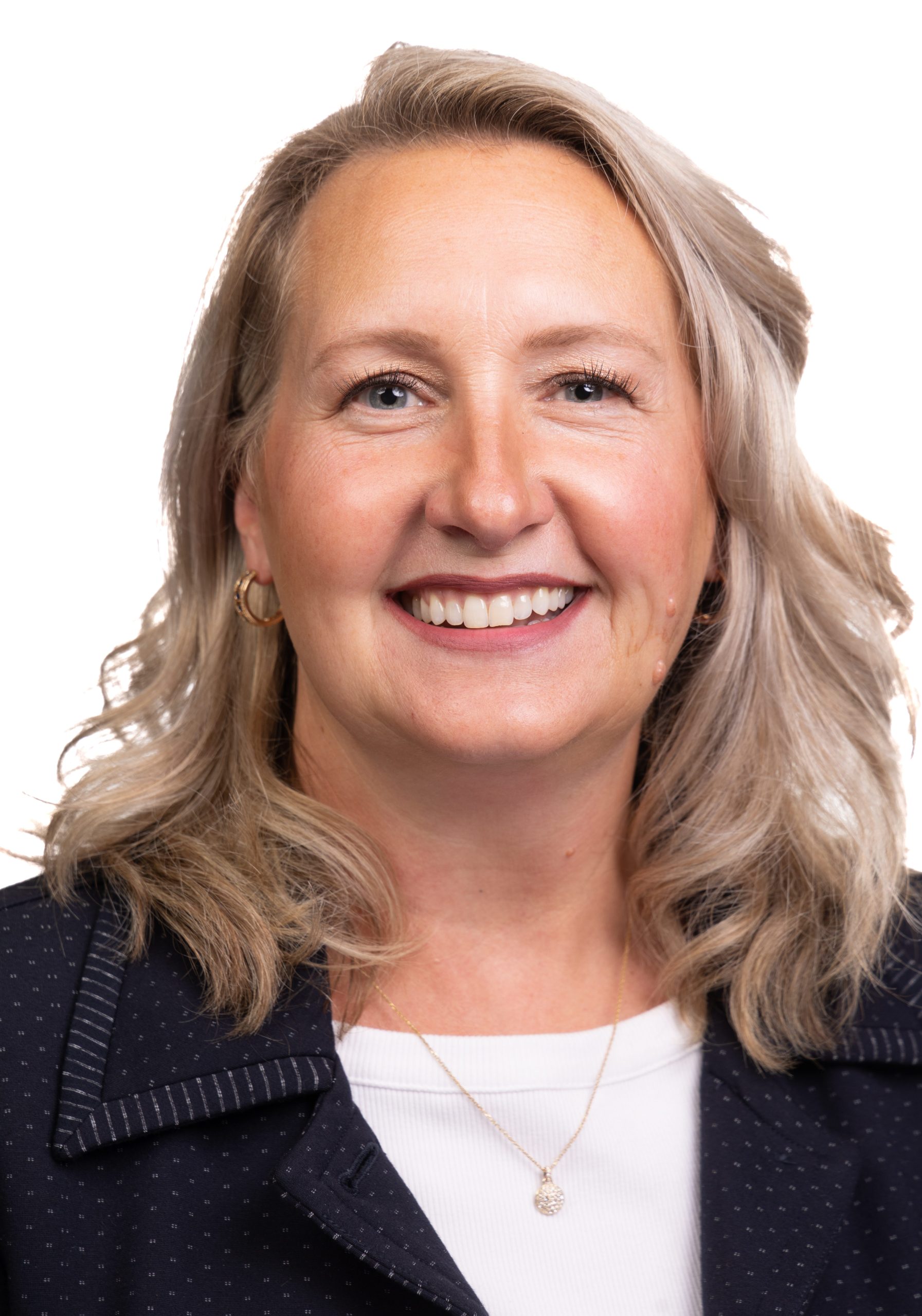 Portrait of a smiling woman with shoulder-length blonde hair wearing a dark blazer over a white top against a white background.