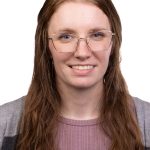 Portrait of a smiling woman with long brown hair and glasses wearing a mauve top and gray cardigan against a white background.