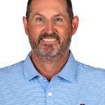 Portrait of a man with a beard wearing a light blue Bushnell Golf polo against a white background.