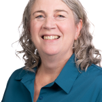 Portrait of a smiling woman wearing a teal collared shirt against a white background.