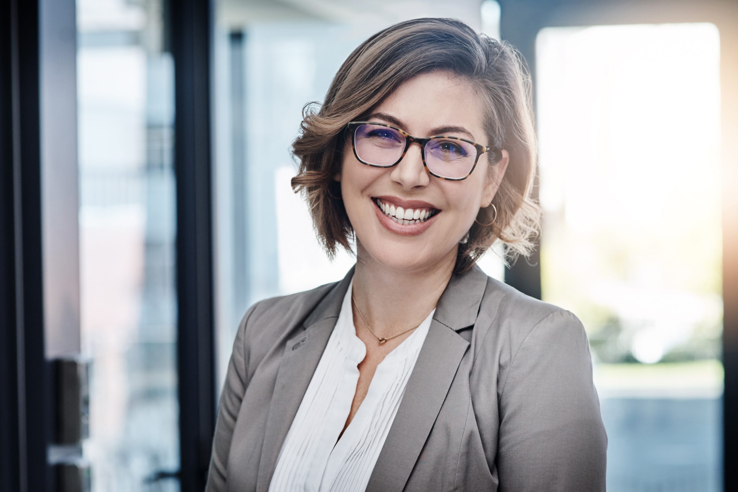AI specialist with glasses and business suit smiles in sunny office.