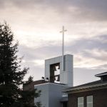 Bushnell University bell tower and cross rising above campus buildings beneath a cloudy sky.