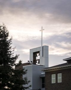 Bushnell University bell tower and cross rising above campus buildings beneath a cloudy sky.