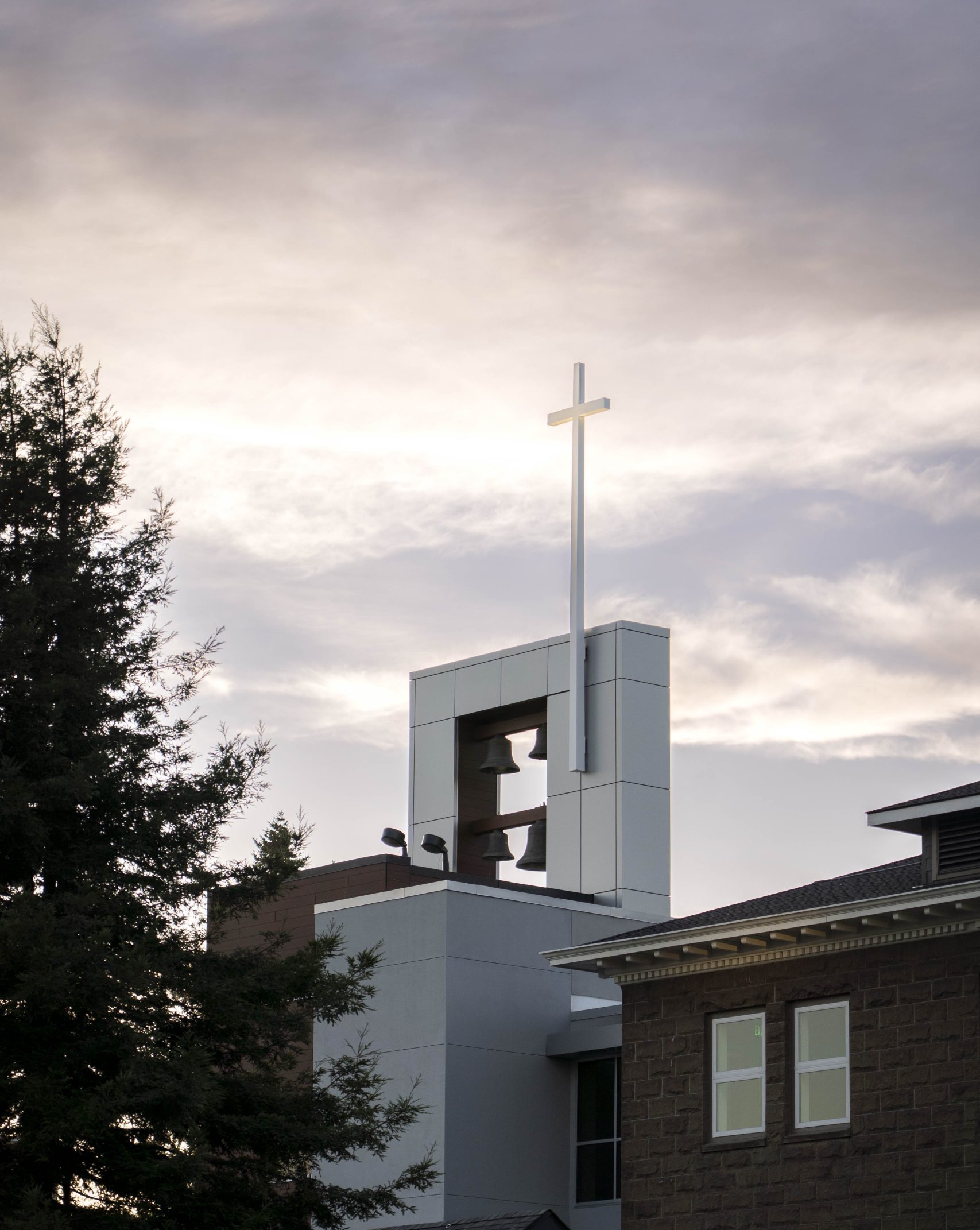 Bushnell University bell tower and cross rising above campus buildings beneath a cloudy sky.