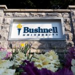 Bushnell University sign surrounded by colorful spring flowers and landscaped greenery.