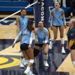 Bushnell University women’s volleyball players celebrate together on the court after sweeping Corban University 3-0.