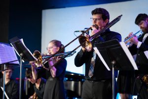 Music students in black formal clothing playing brass instruments during a concert.