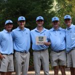 Five Bushnell University men's golf team members pose in matching light blue polos and caps, holding a Tall Timber Invitational men's team championship award.