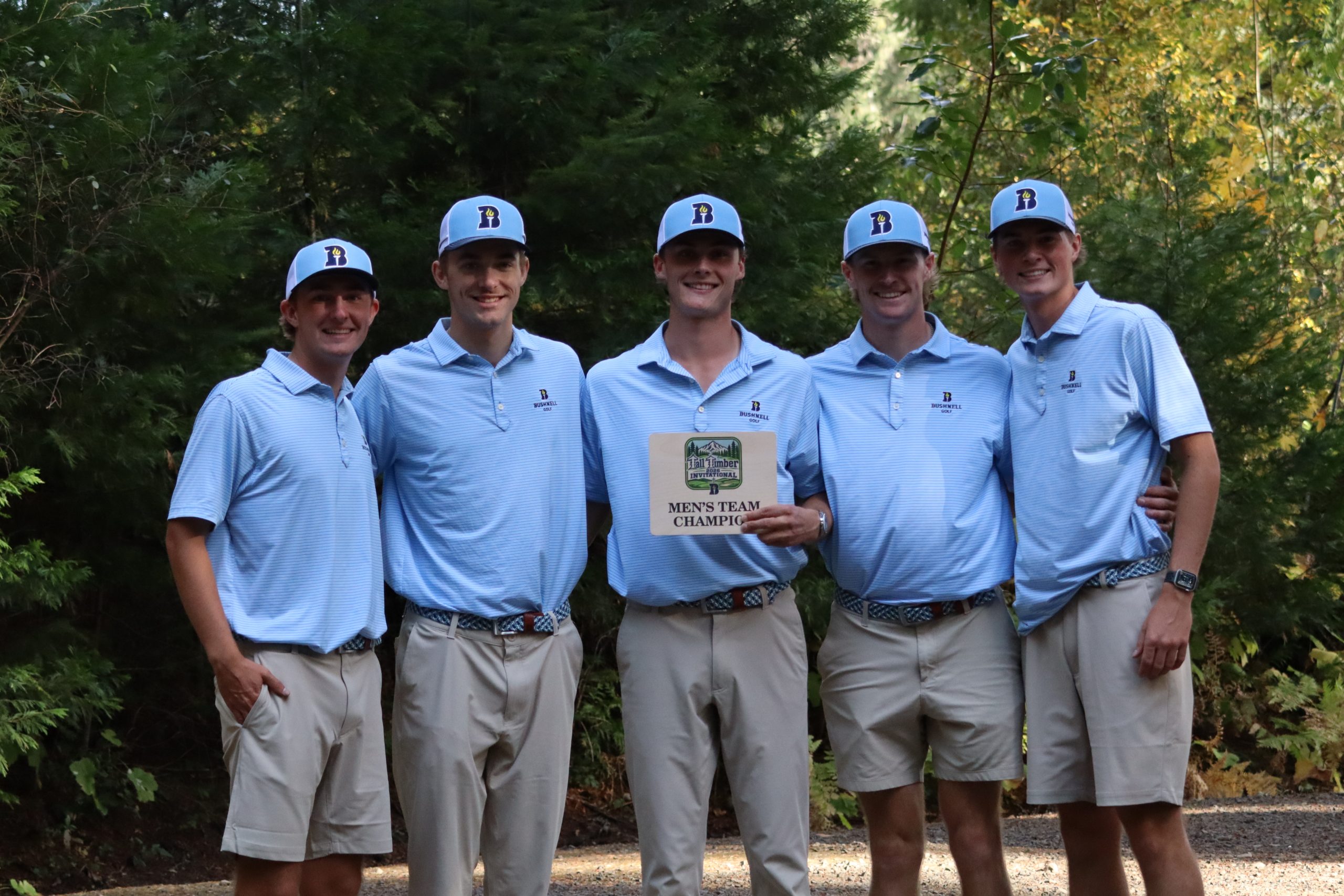 Five Bushnell University men's golf team members pose in matching light blue polos and caps, holding a Tall Timber Invitational men's team championship award.