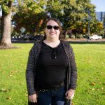 Portrait of Andrea Niemeyer smiling outdoors on the Bushnell University campus, wearing sunglasses, a black top and gray cardigan.
