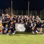 Bushnell University men's soccer players and coaches celebrate a 2025 Cascade Collegiate Conference tournament victory, posing together around a championship bracket on the field at night.